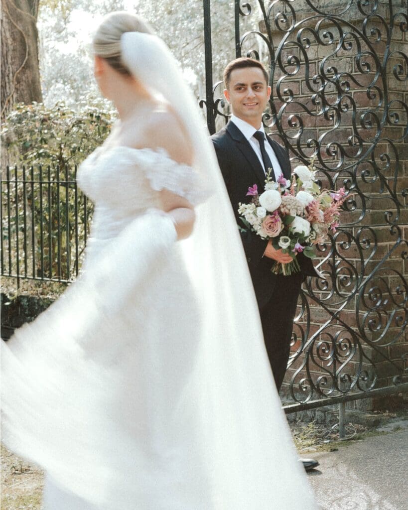 A groom looks at his bride in front of an iron gate during a romantic, fairytale elopement in Asheville.
