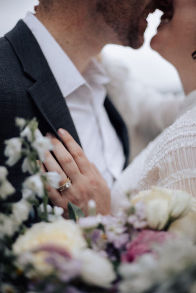 A bride and groom kiss holding a bouquet of flowers at the North Carolina Arboretum.