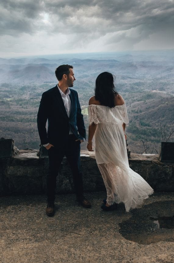 A bride and groom at Pretty Place in Greenville, look out over a cloudy mountain view.