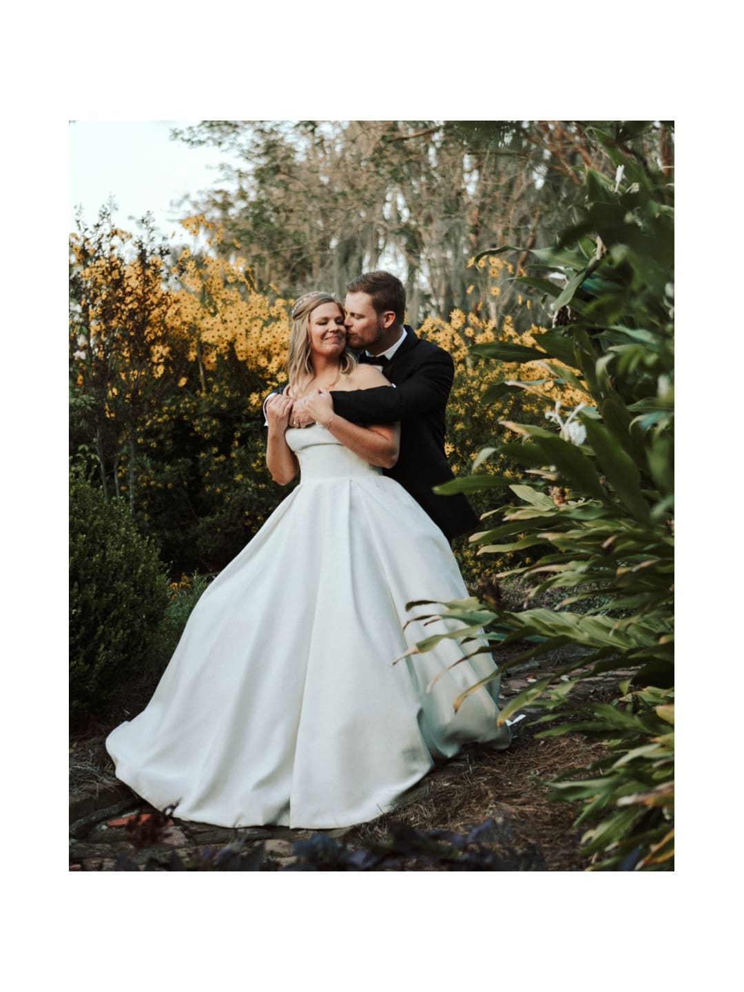 An eloping couple embraces in a park surrounded by yellow flowers