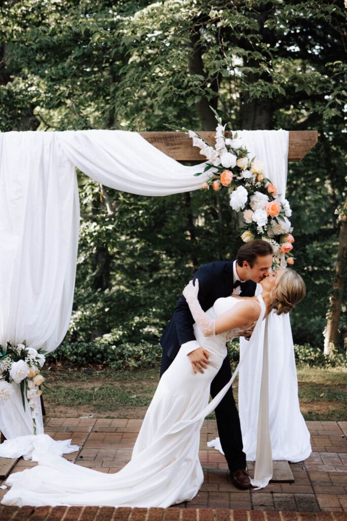 A bride and groom kiss in front of their arbor.