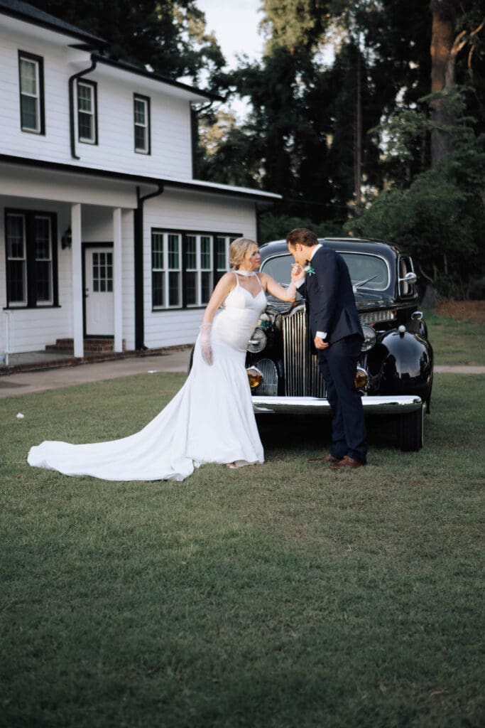 A bride and groom stand in front of a vintage car at their Greenville Wedding Venue.